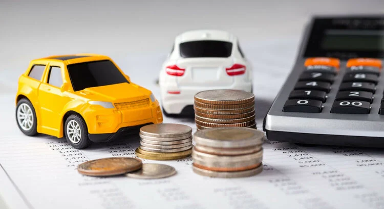 Deux petits modèles de voitures et des piles de pièces sont placés sur un document financier à côté d'une calculatrice.