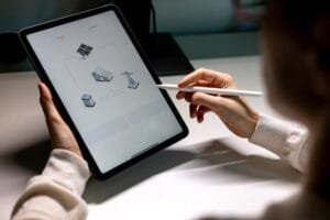 Une personne utilise un stylet sur une tablette affichant un schéma représentant des panneaux solaires, une maison, une batterie et un réseau électrique.