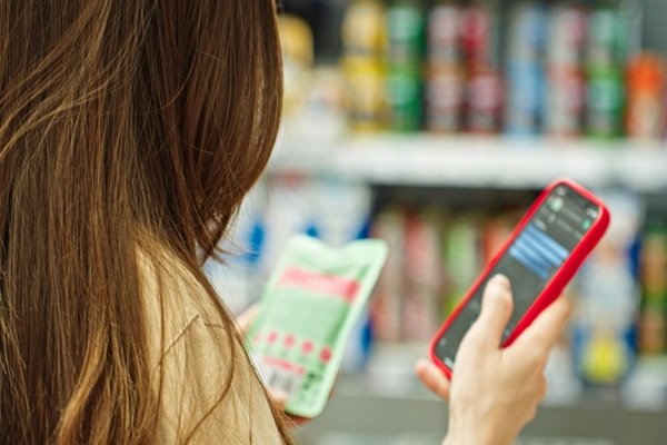 Une personne tenant un smartphone et un sachet de nourriture dans l'allée d'un supermarché.