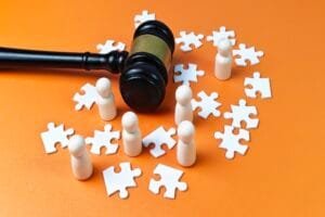 Un marteau de juge entouré de poupées en bois et de pièces de puzzle blanches éparpillées sur une surface orange.