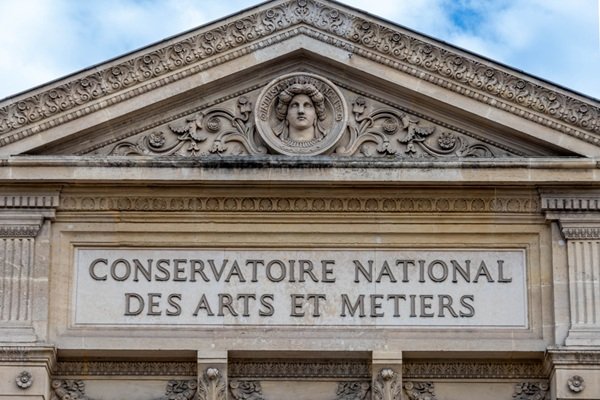 Fronton en pierre du Conservatoire national des arts et métiers, orné d'un médaillon central représentant un visage sculpté.