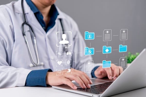 Un médecin en blouse blanche tapant sur un ordinateur portable, avec une interface numérique composée d'icônes médicales et de dossiers de patients flottant au-dessus du clavier.