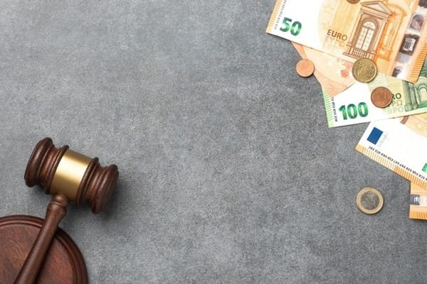 Un marteau de bois muni d'un bloc de résonance, posé à côté de divers billets et pièces en euros sur une surface grise.