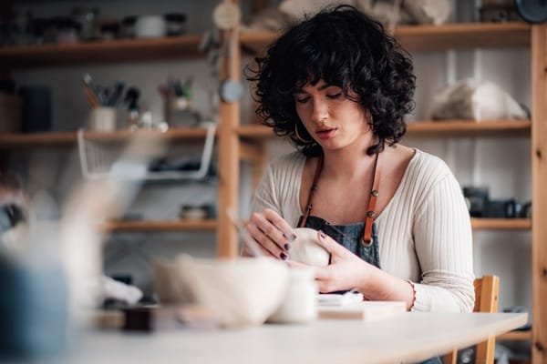 Une personne portant un tablier façonne un morceau d'argile sur une table dans un atelier de poterie.