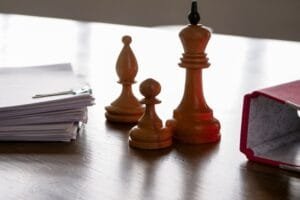 Une pile de papiers, un fou, un pion, un roi et un dossier ouvert sur un bureau.