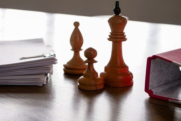 Une pile de papiers, un fou, un pion, un roi et un dossier ouvert sur un bureau.