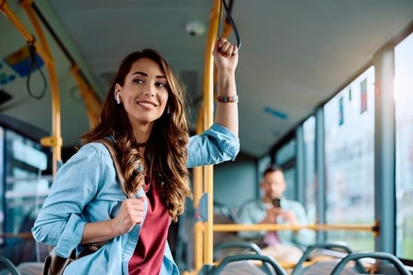 Une femme souriante, équipée d'écouteurs, tient une sangle de sécurité tout en restant debout dans un bus.