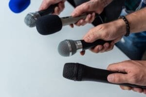 Quatre mains tenant des microphones et les dirigeant vers un orateur hors champ.