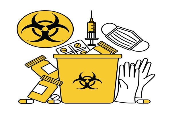 Un conteneur pour déchets à risque biologique entouré de matériel médical, notamment une seringue, un masque, des gants et des flacons de médicaments.