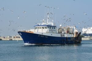 Un bateau de pêche bleu et blanc naviguant dans un port, entouré d'une nuée de mouettes.
