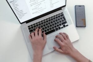 Une personne qui tape sur un ordinateur portable, tandis qu'une application de calculatrice est ouverte sur un smartphone posé à proximité.